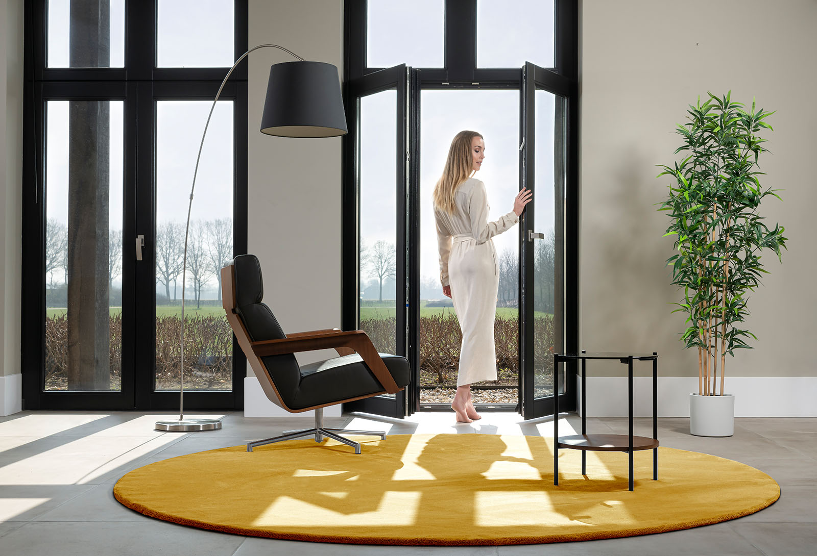 Vrouw kijkt om naar rond geel vloerkleed vanuit deuropening